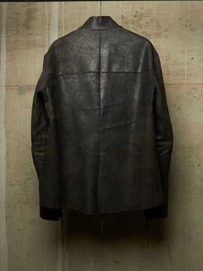 A dark charcoal gray distressed leather jacket shown from the back, hanging against a textured concrete wall.
