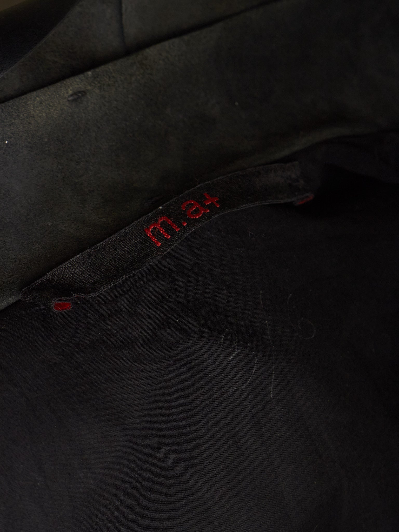 Close-up of a black fabric garment with red embroidered 'm.4' text on a black fabric label.