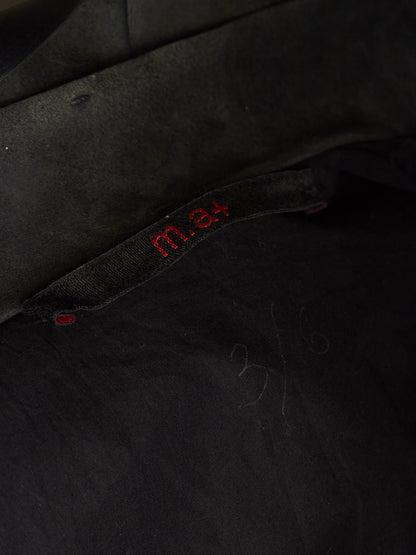 Close-up of a black fabric garment with red embroidered 'm.4' text on a black fabric label.
