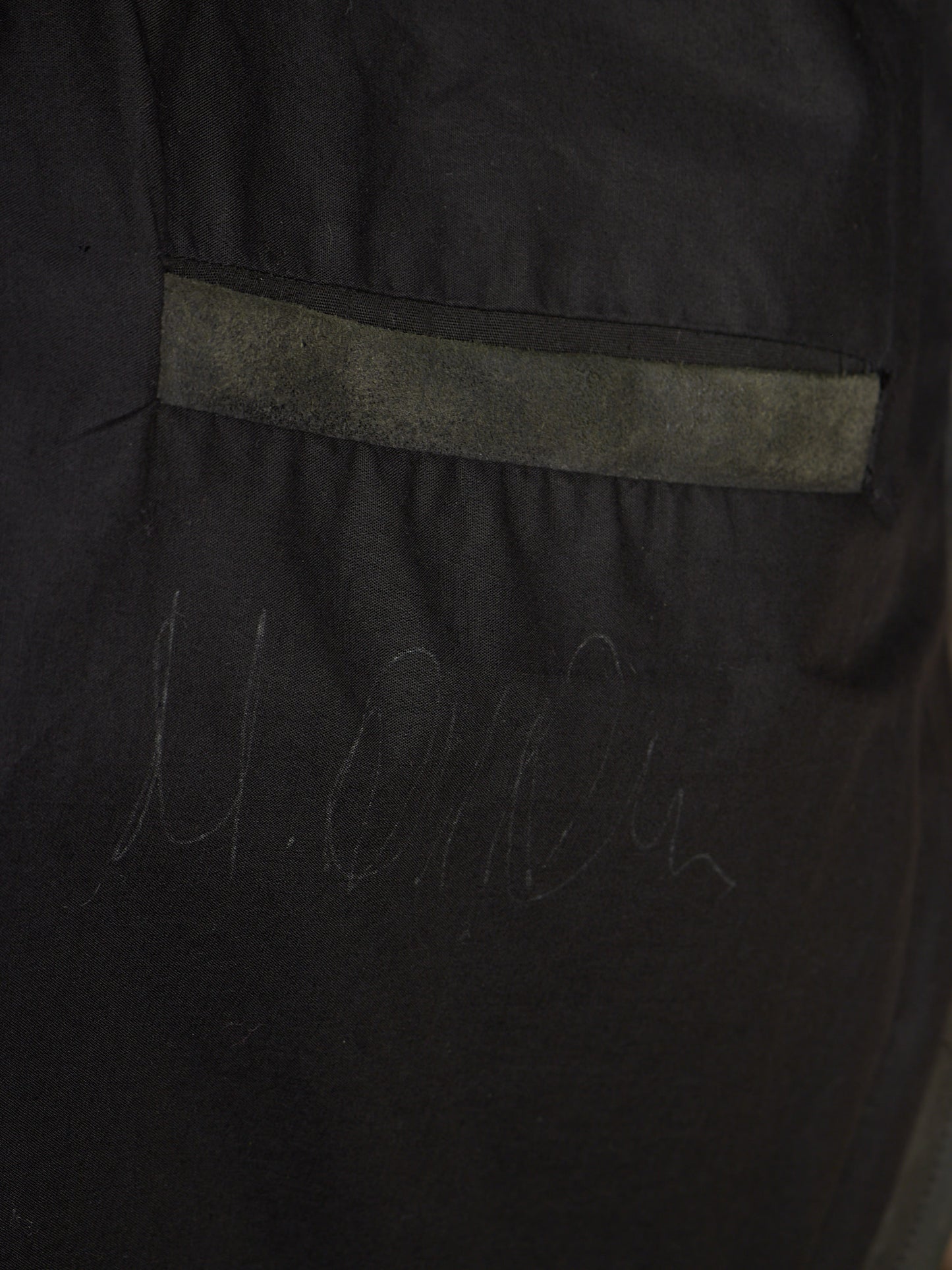 Close-up of a black garment or fabric panel with a horizontal gray stitched stripe and faint gray script marking near the bottom.