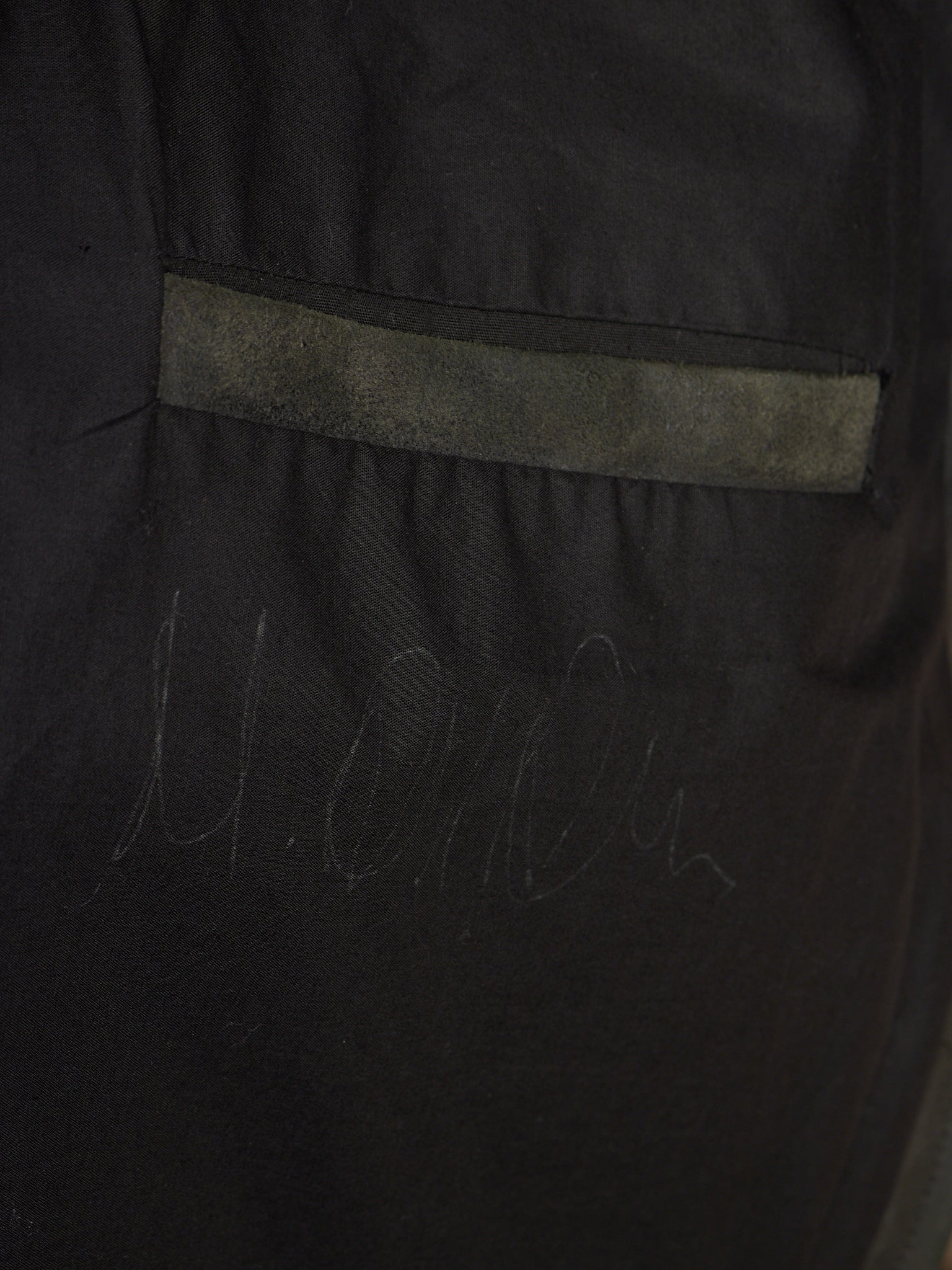 Close-up of a black garment or fabric panel with a horizontal gray stitched stripe and faint gray script marking near the bottom.