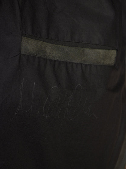 Close-up of a black garment or fabric panel with a horizontal gray stitched stripe and faint gray script marking near the bottom.