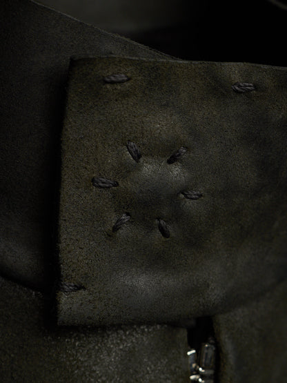 Close-up of a dark olive green leather strap or cuff with decorative whipstitching and a small silver metal clasp visible at the bottom edge.