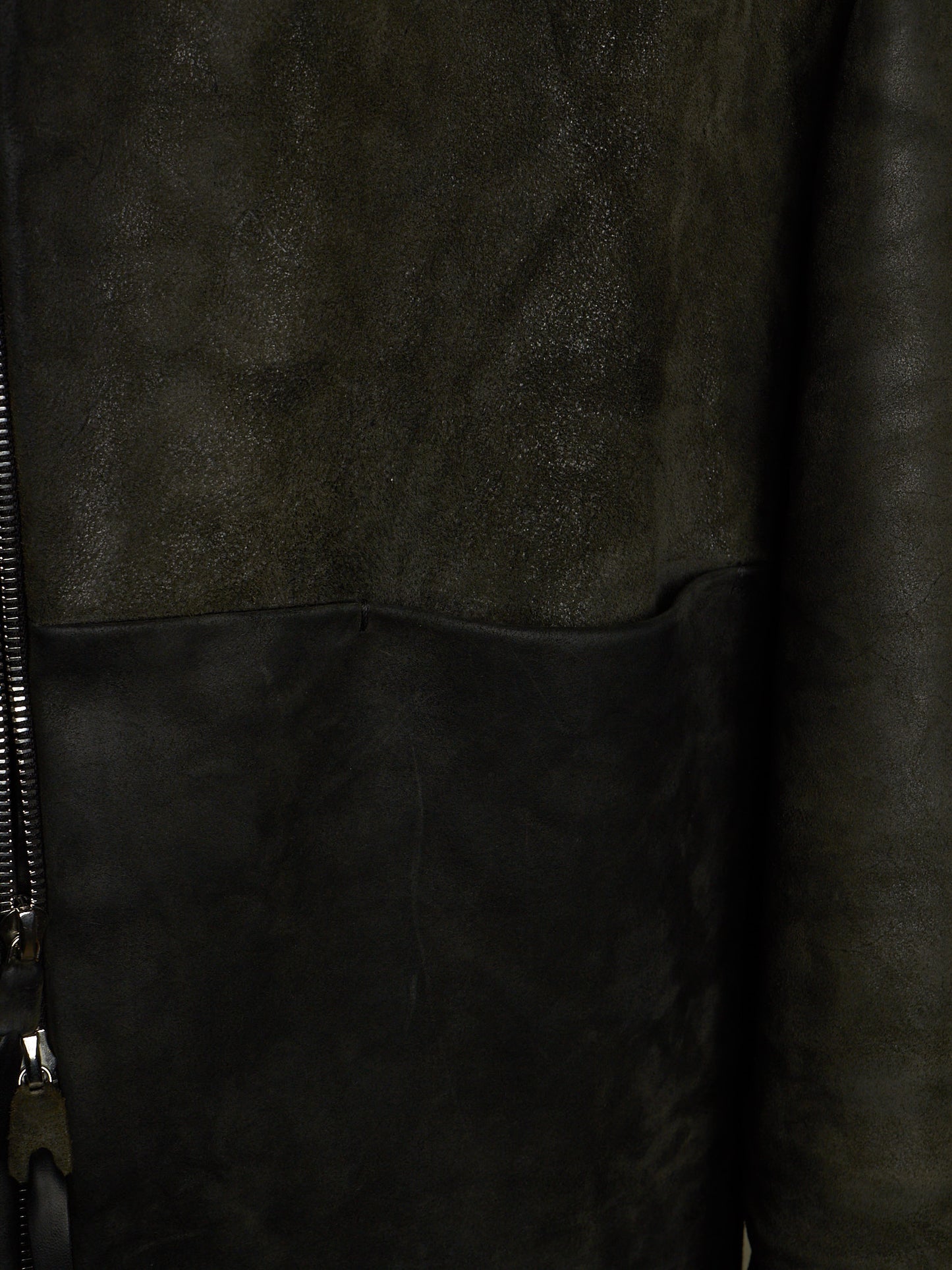 Close-up of a dark brown leather jacket showing a textured suede-like upper panel, smooth leather lower panel, and a black zipper on the left side.