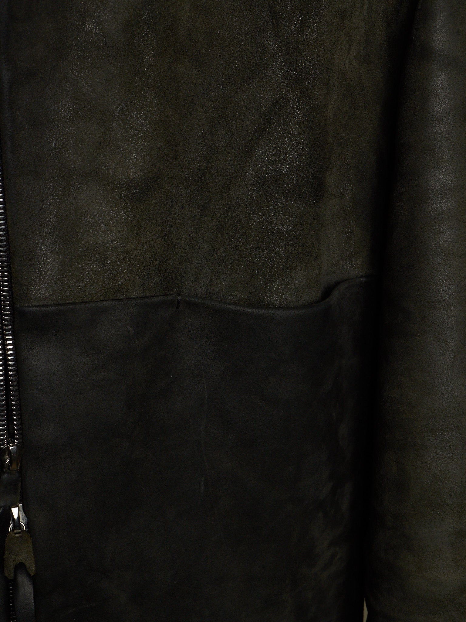 Close-up of a dark brown leather jacket showing a textured suede-like upper panel, smooth leather lower panel, and a black zipper on the left side.