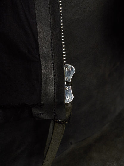 Close-up of a black leather jacket with a silver metal zipper and a decorative silver zipper pull featuring the brand name 'MUT'.
