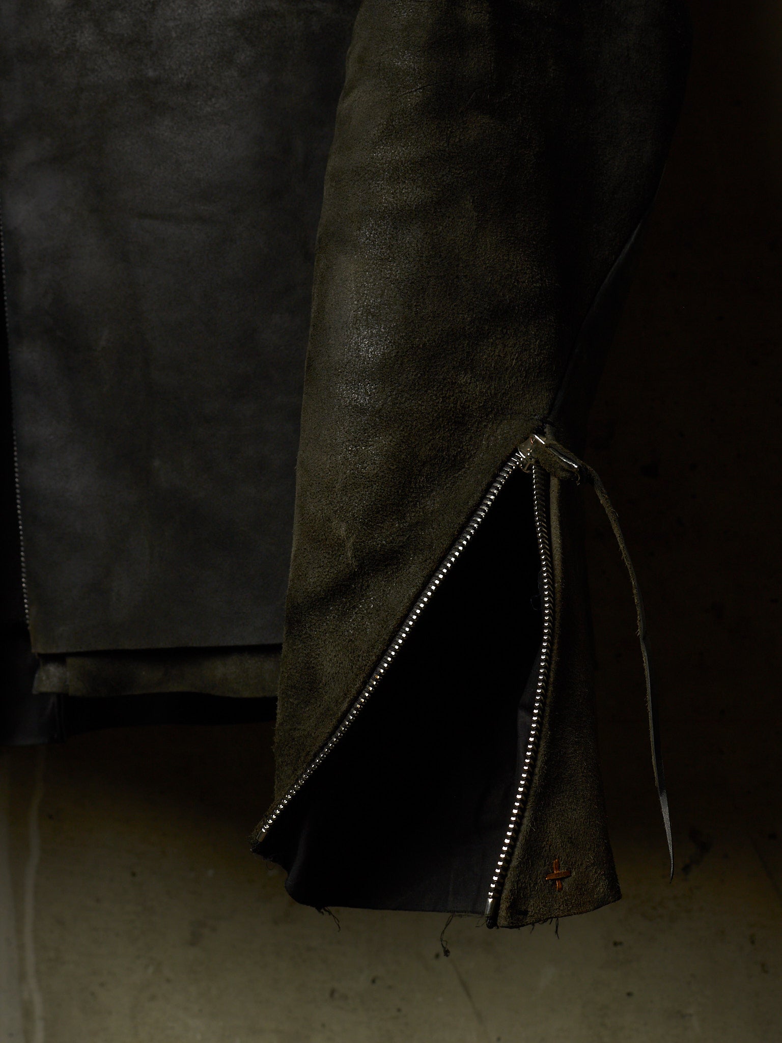A close-up of a dark brown leather jacket with a silver zipper detail and a drawstring, set against a dark background.