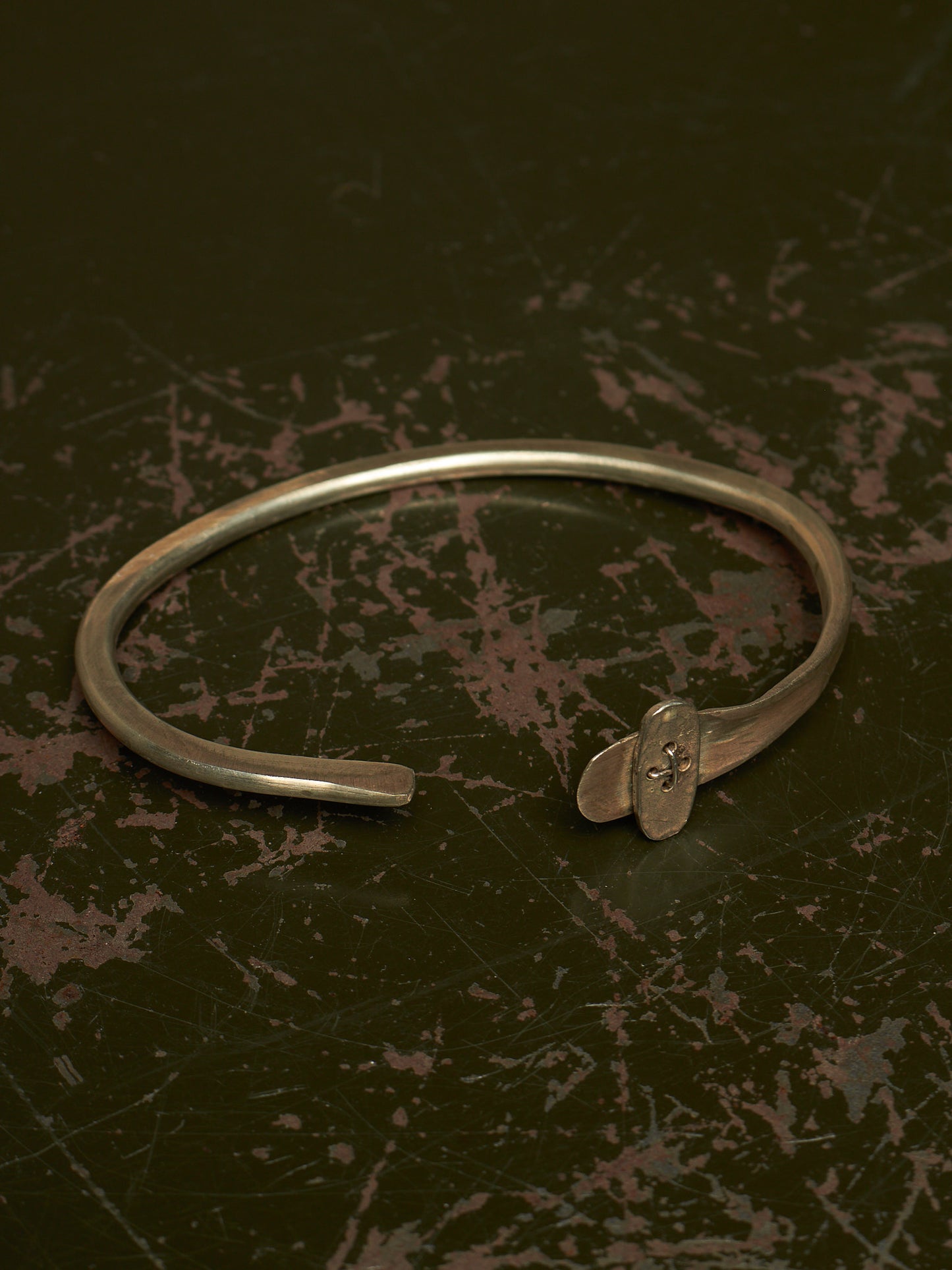 A silver-toned metal cuff bracelet with a small decorative element at the open end, photographed on a dark textured surface.