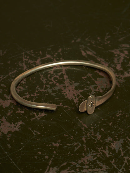 A silver-toned metal cuff bracelet with a small decorative element at the open end, photographed on a dark textured surface.
