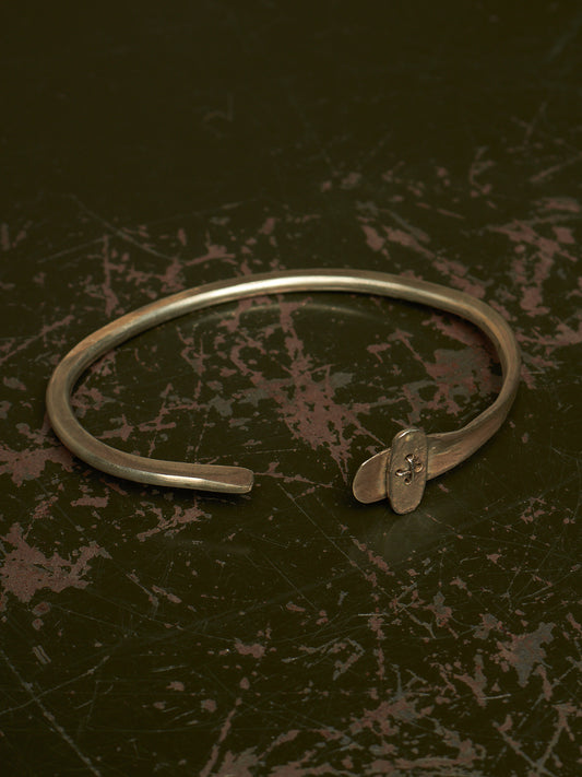 A silver-toned metal cuff bracelet with a small decorative element at the open end, photographed on a dark textured surface.