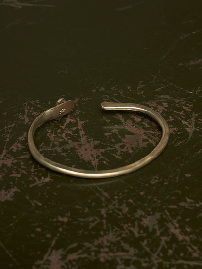 A thin silver-toned metal cuff bracelet with a small engraved symbol on the inside, displayed on a dark textured surface.