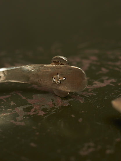 A close-up of a silver metal spoon handle with a small engraved anchor symbol, resting on a dark, textured surface.