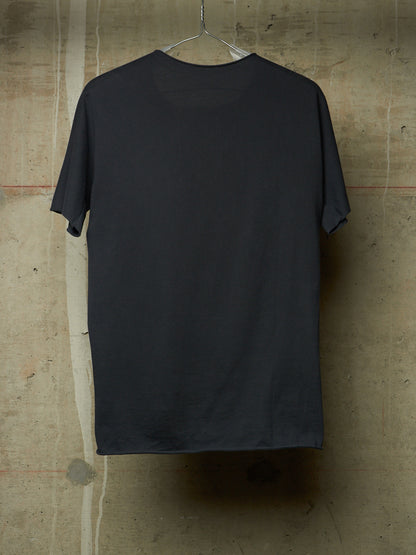 A dark charcoal gray short-sleeve t-shirt hanging on a clear plastic hanger against a textured concrete wall.