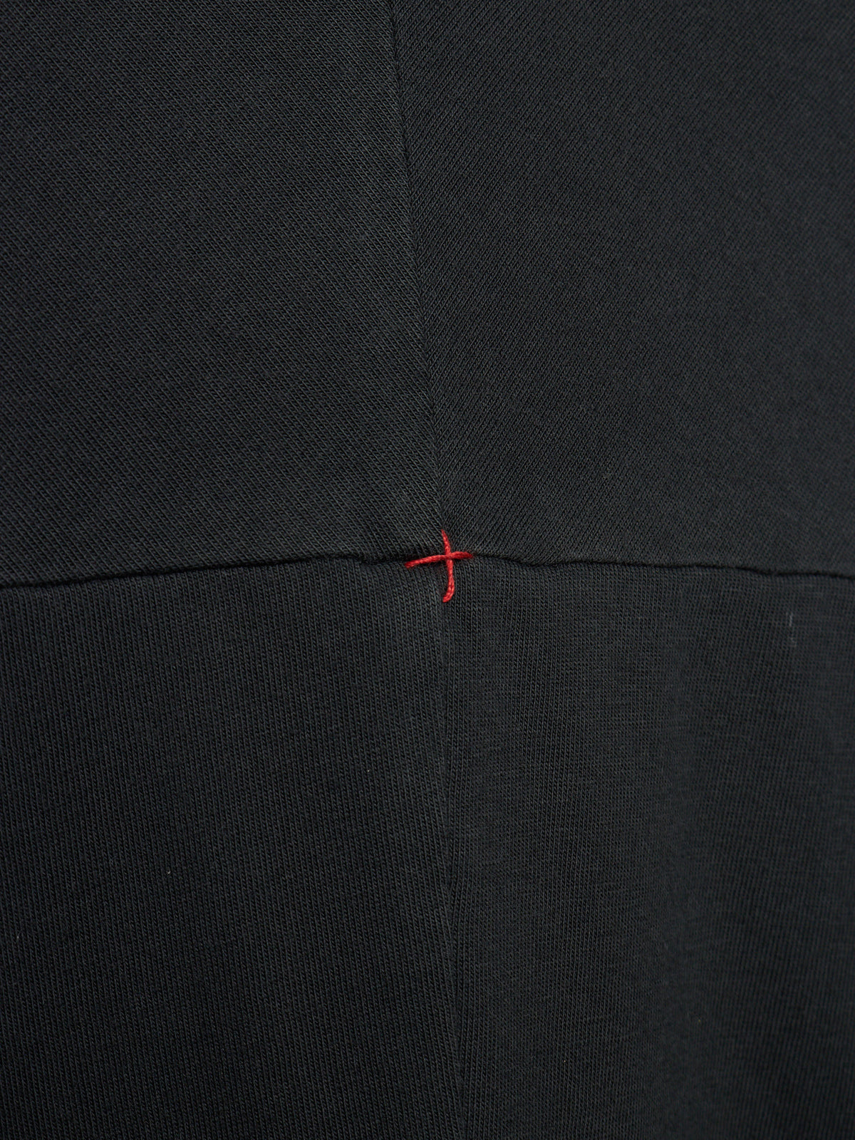 Close-up of a black textured fabric with a central horizontal seam and a small red stitched cross detail at the intersection.