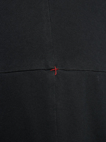 Close-up of a black textured fabric with a central horizontal seam and a small red stitched cross detail at the intersection.