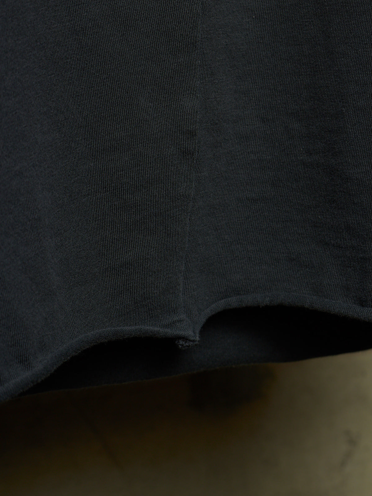 Close-up detail of a dark charcoal gray knit fabric garment, showing the texture and a curved hemline.