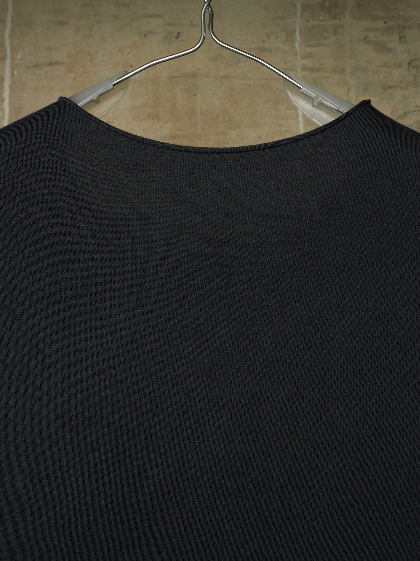 A close-up of a black ribbed knit top hanging on a clear plastic hanger against a beige tiled wall.