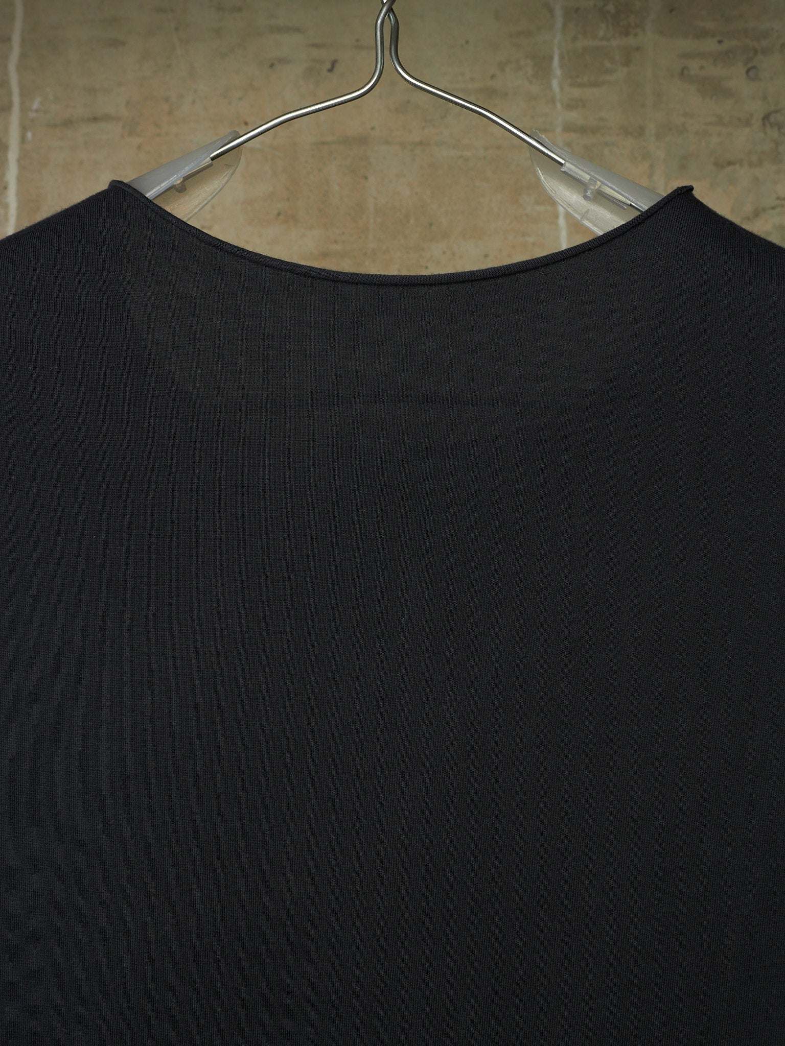 A close-up of a black ribbed knit top hanging on a clear plastic hanger against a beige tiled wall.