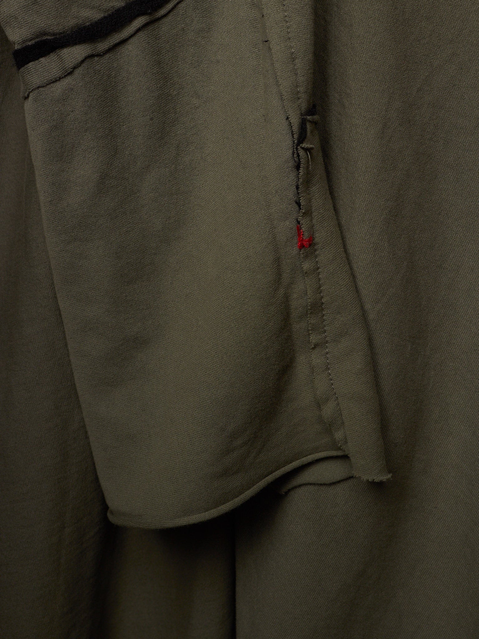 Close-up of olive green fabric with a small red accent stitch detail.