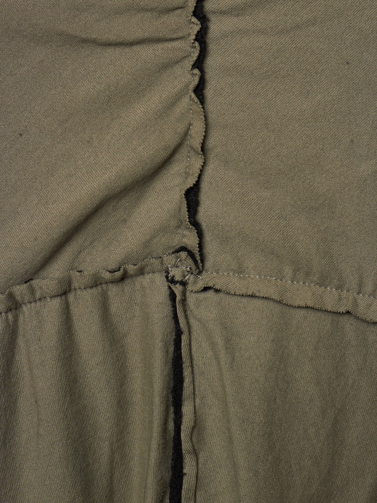 Close-up of olive green fabric with a gathered vertical seam and a horizontal stitched seam, showing the texture and construction details.