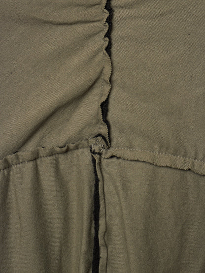 Close-up of olive green fabric with a gathered vertical seam and a horizontal stitched seam, showing the texture and construction details.