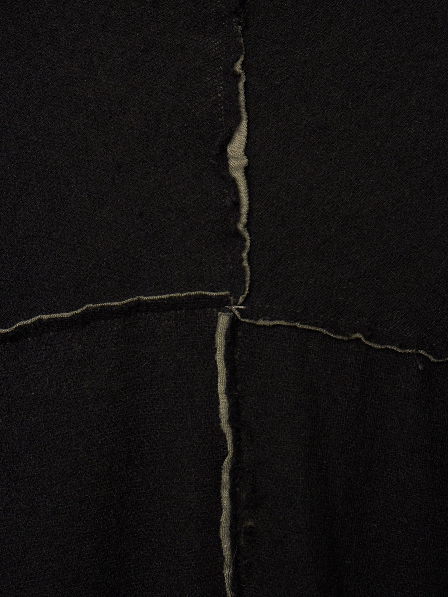 A close-up of a black textile surface with a visible vertical and horizontal seam forming an X shape, showing the raw, slightly frayed edges of the fabric.