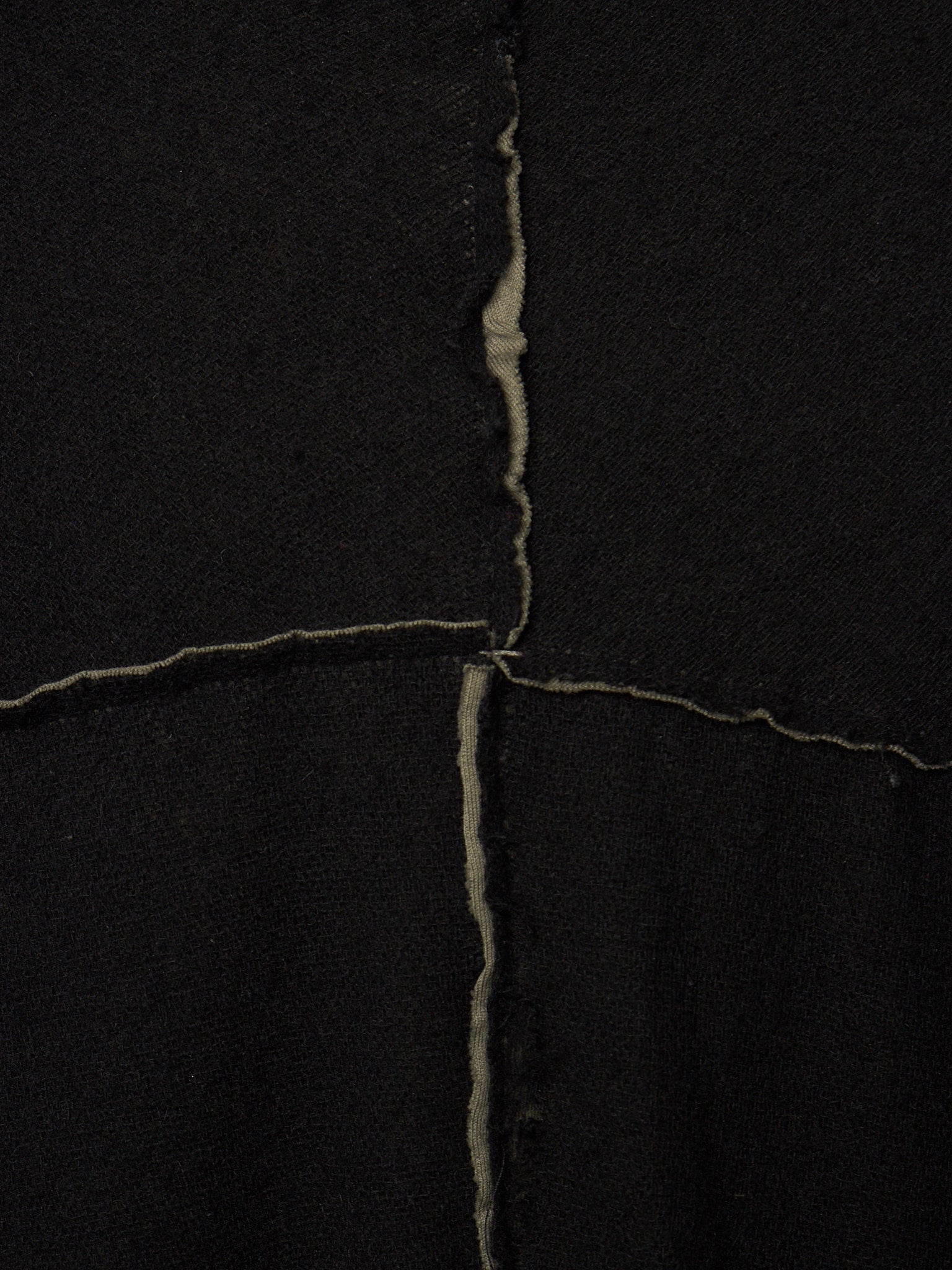A close-up of a black textile surface with a visible vertical and horizontal seam forming an X shape, showing the raw, slightly frayed edges of the fabric.