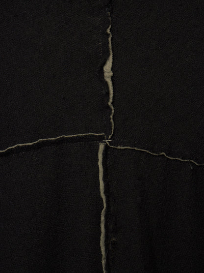 A close-up of a black textile surface with a visible vertical and horizontal seam forming an X shape, showing the raw, slightly frayed edges of the fabric.