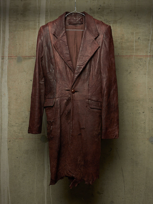 A distressed, heavily textured brown leather coat hanging on a wire hanger against a concrete wall.
