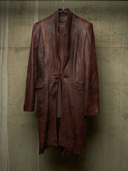 A distressed, dark reddish-brown leather coat hanging on a wire hanger against a textured concrete wall.