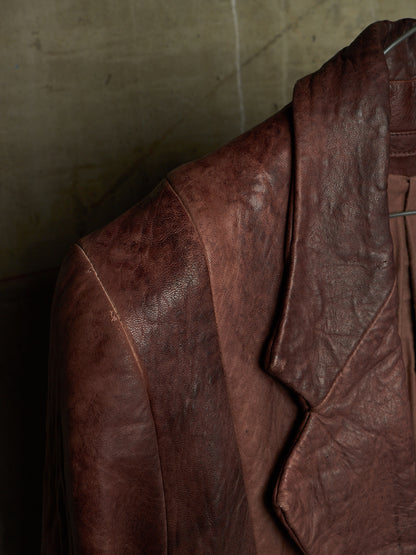 A close-up of a distressed brown leather jacket hanging against a textured concrete wall.
