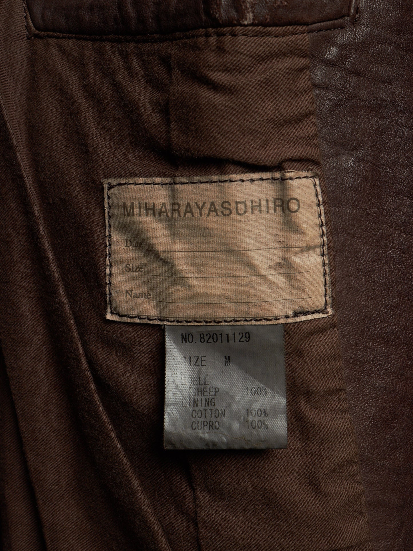 Close-up of the inside of a brown jacket showing a sewn-in label reading MIHARAYASUHIRO and a smaller size tag below it.