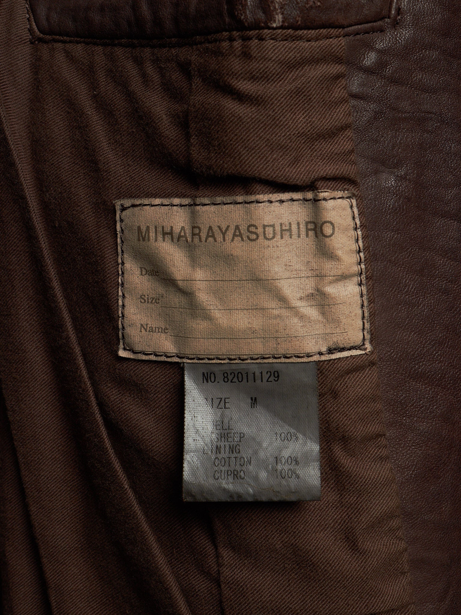 Close-up of the inside of a brown jacket showing a sewn-in label reading MIHARAYASUHIRO and a smaller size tag below it.