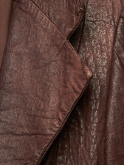 A close-up of a brown leather jacket showing the textured, crinkled leather material and a diagonal fold.