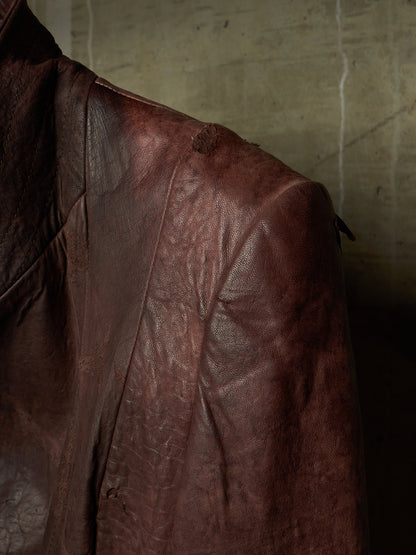 A close-up of a distressed brown leather jacket, showing the textured leather fabric and shoulder detail against a dark, moody background.