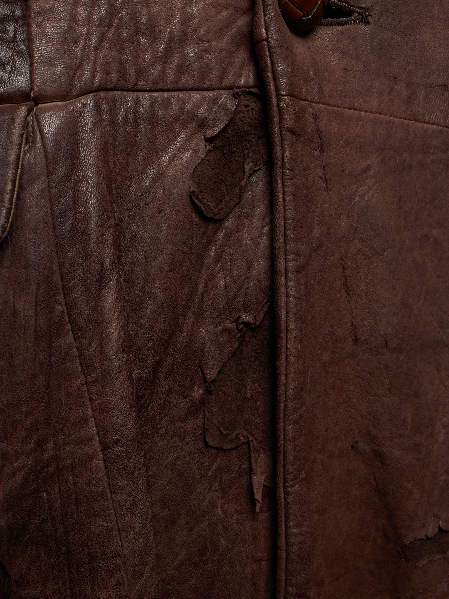 Close-up of a dark brown distressed leather jacket showing the texture, creases, and frayed edges.