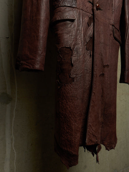 A dark brown distressed leather coat with heavy rips and tattered edges, hanging against a textured concrete wall.