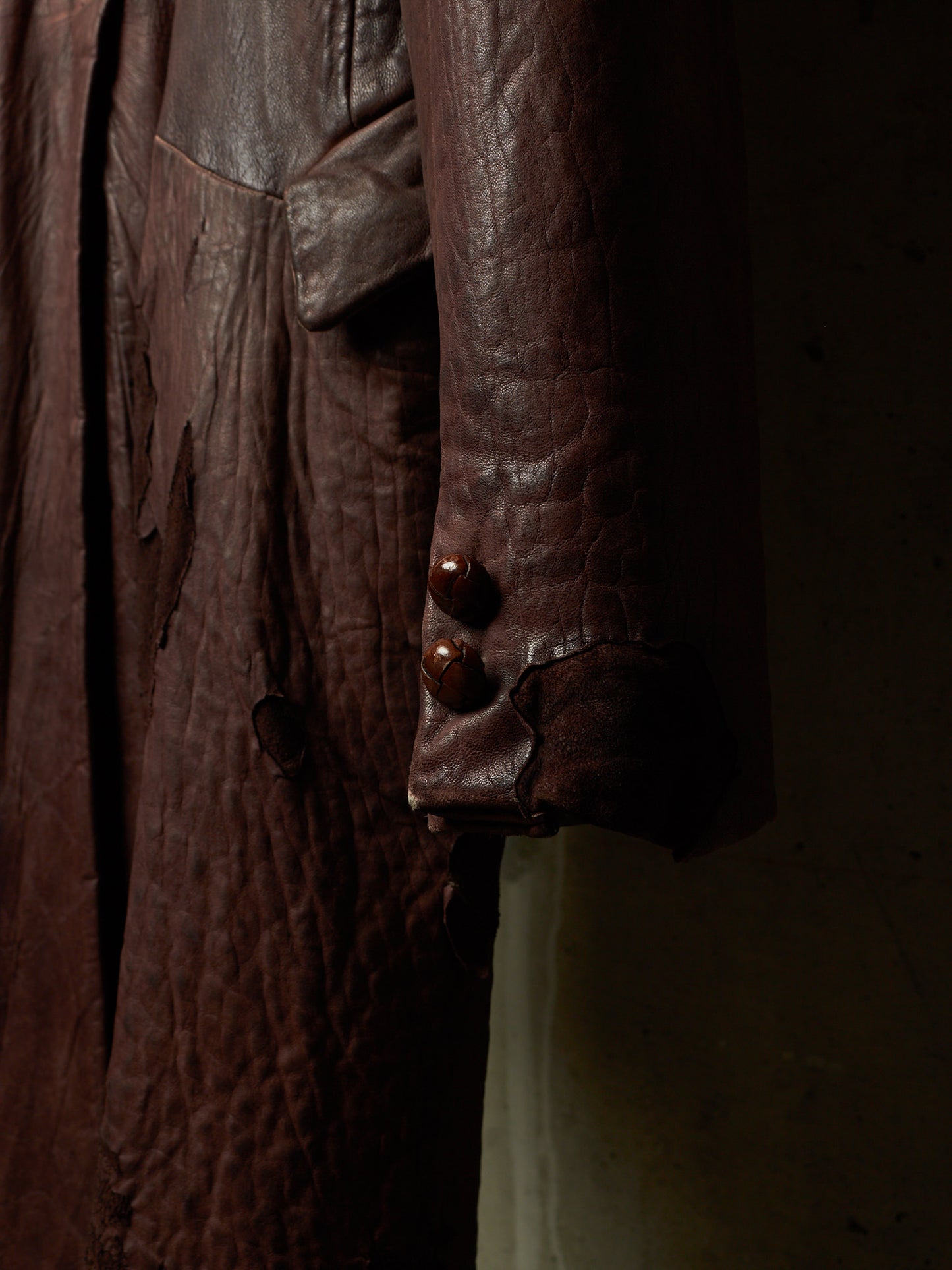 Close-up of a dark brown textured leather jacket with two prominent brown buttons on the cuff, set against a dark background.