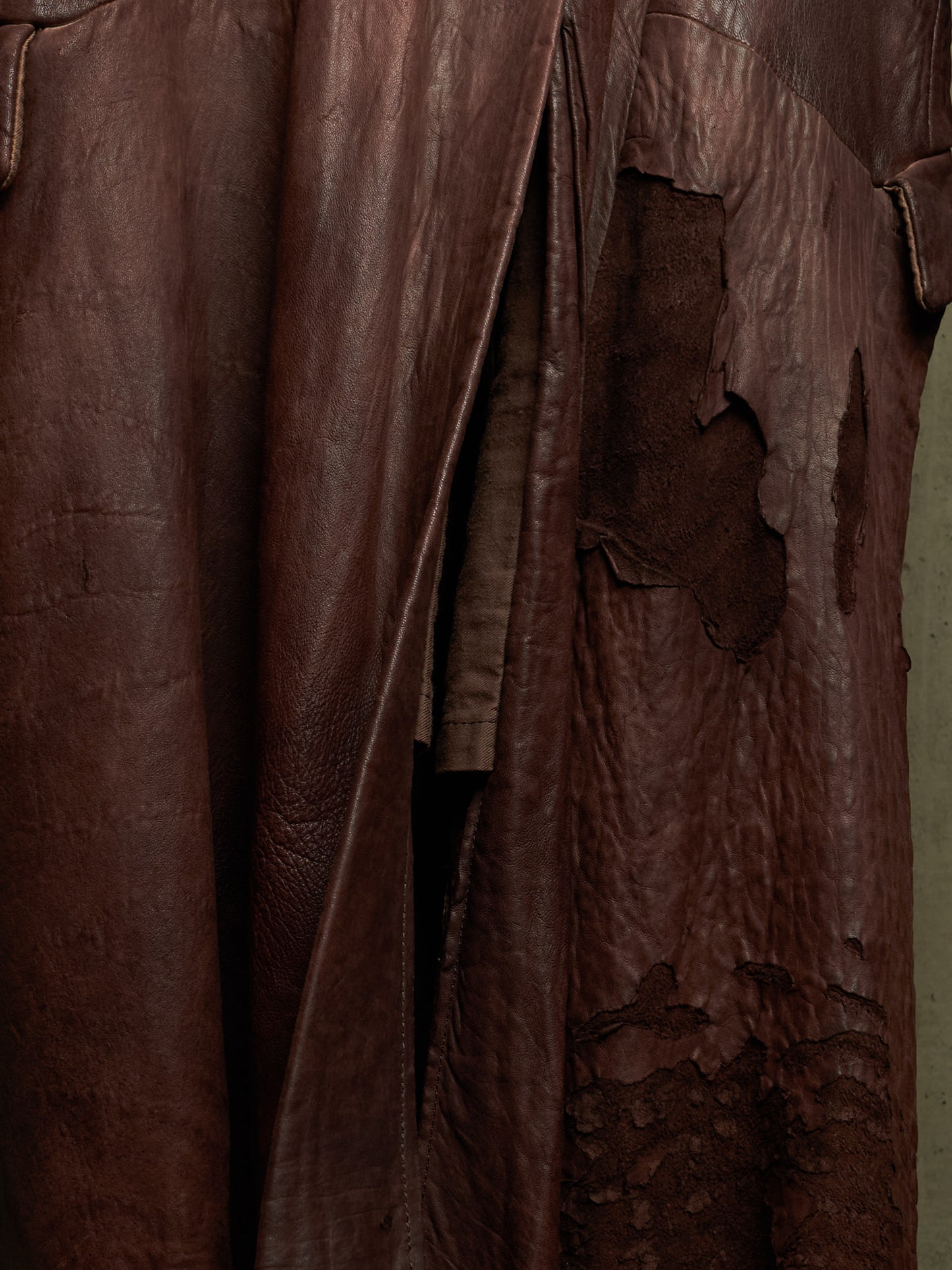 A close-up of a dark brown distressed leather garment, showing textured folds, creases, and peeling sections of the leather surface.