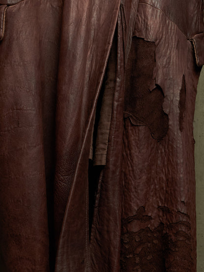 A close-up of a dark brown distressed leather garment, showing textured folds, creases, and peeling sections of the leather surface.