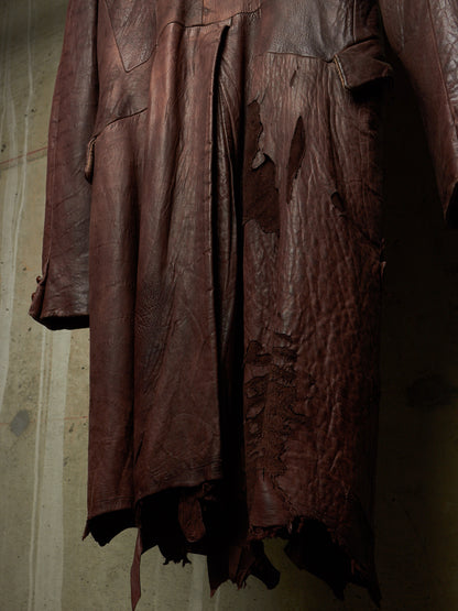 A dark reddish-brown distressed leather coat or jacket hanging against a textured concrete wall.