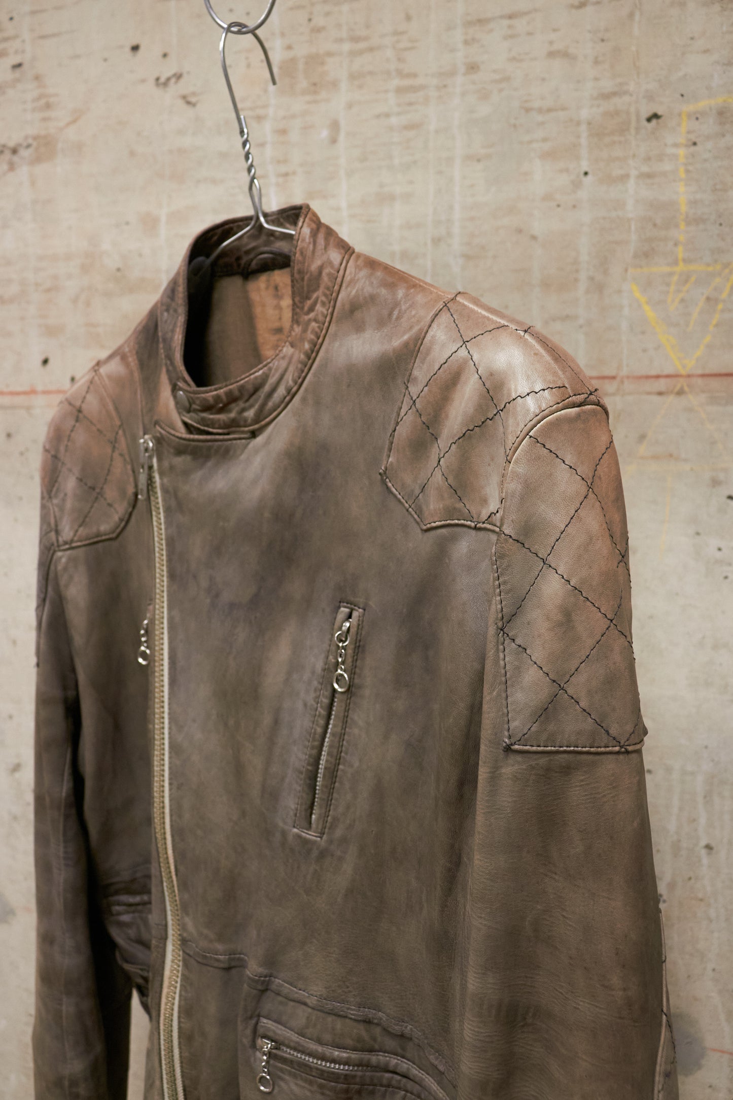 Brown leather jacket hanging on a hook against a textured wall.