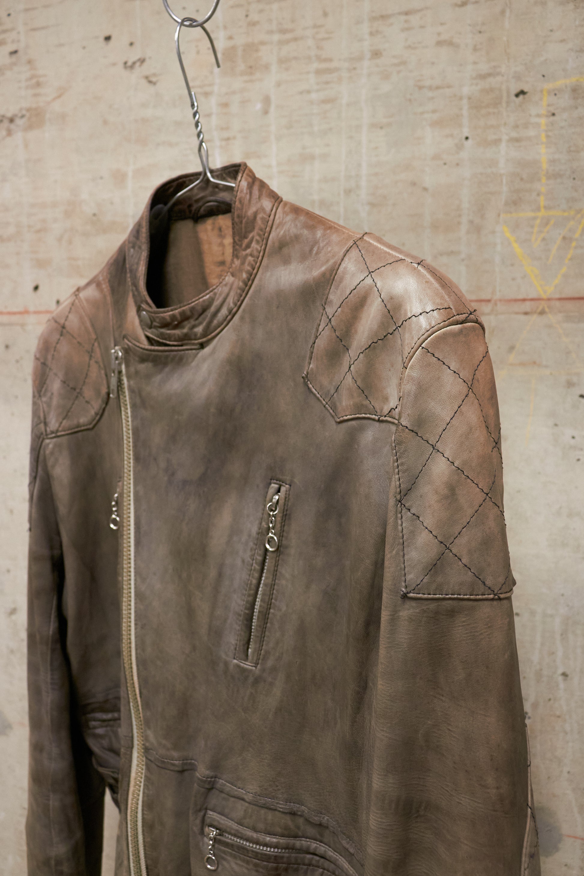 Brown leather jacket hanging on a hook against a textured wall.