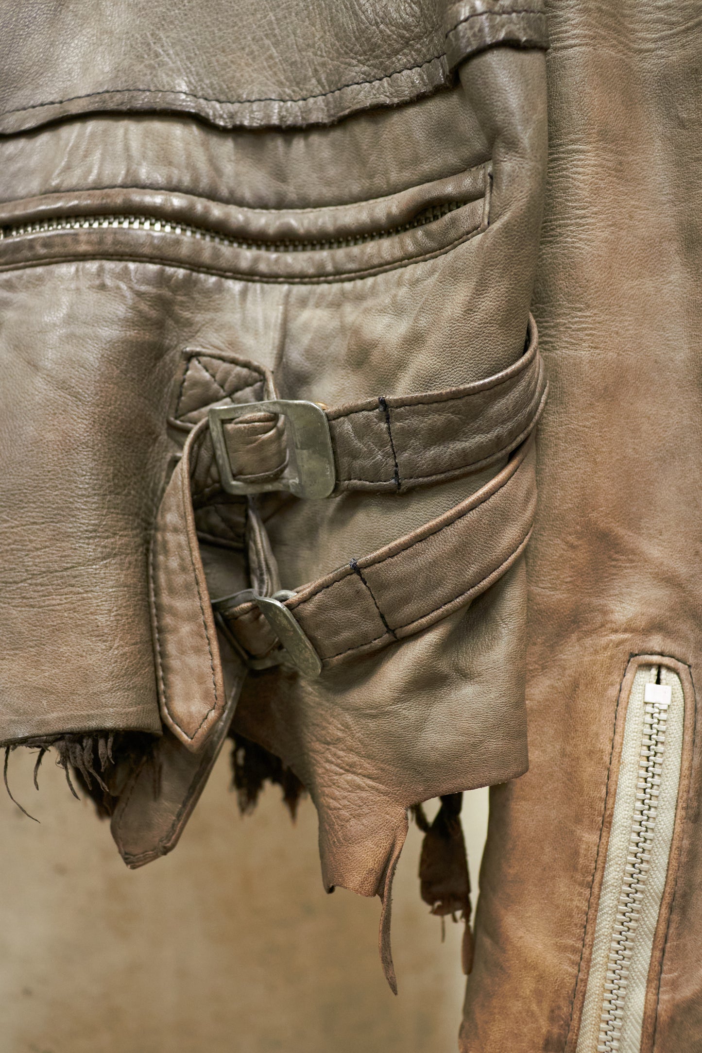 Close-up of a brown leather jacket with a belt and zipper details.