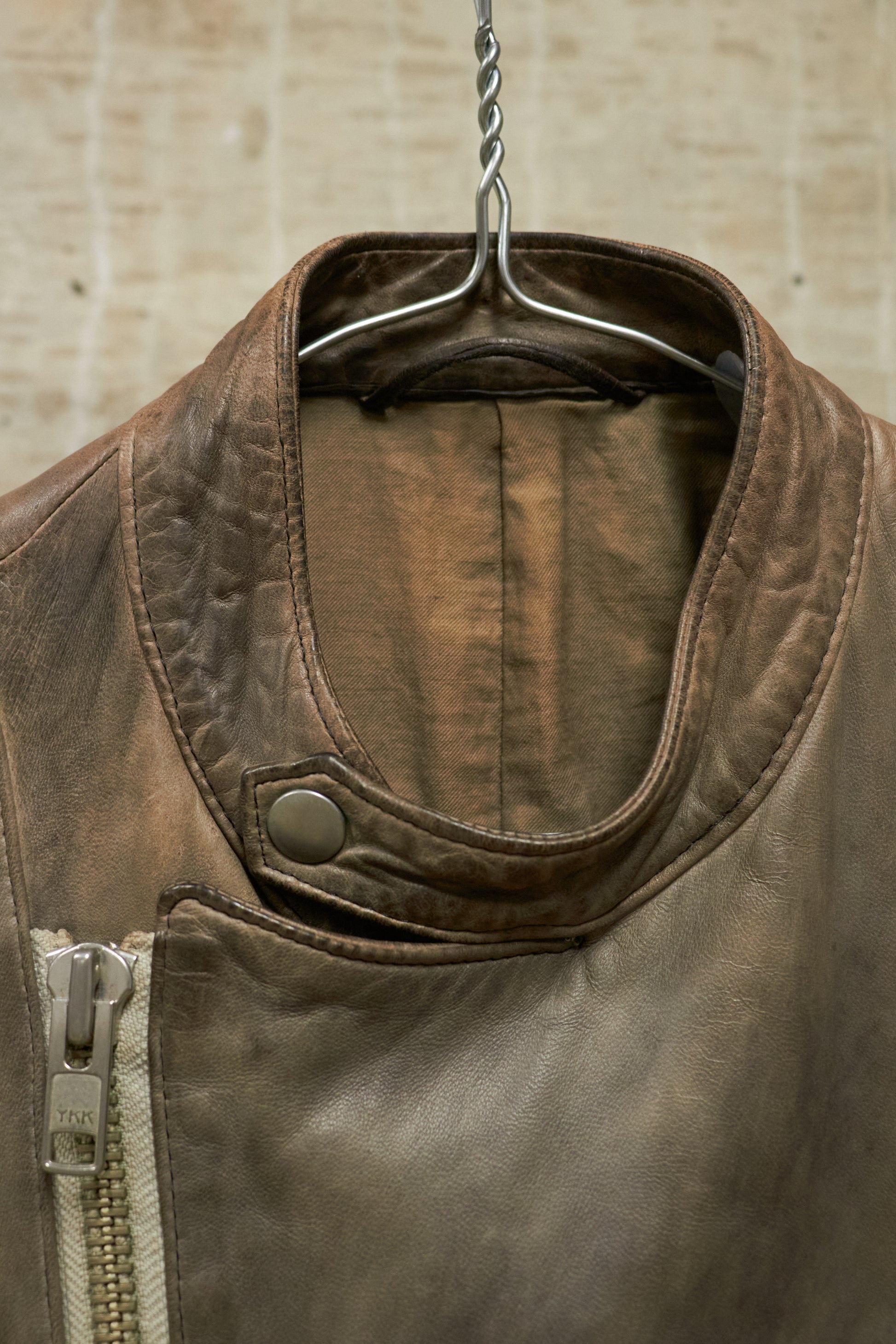 Brown leather jacket on a hanger against a beige wall.