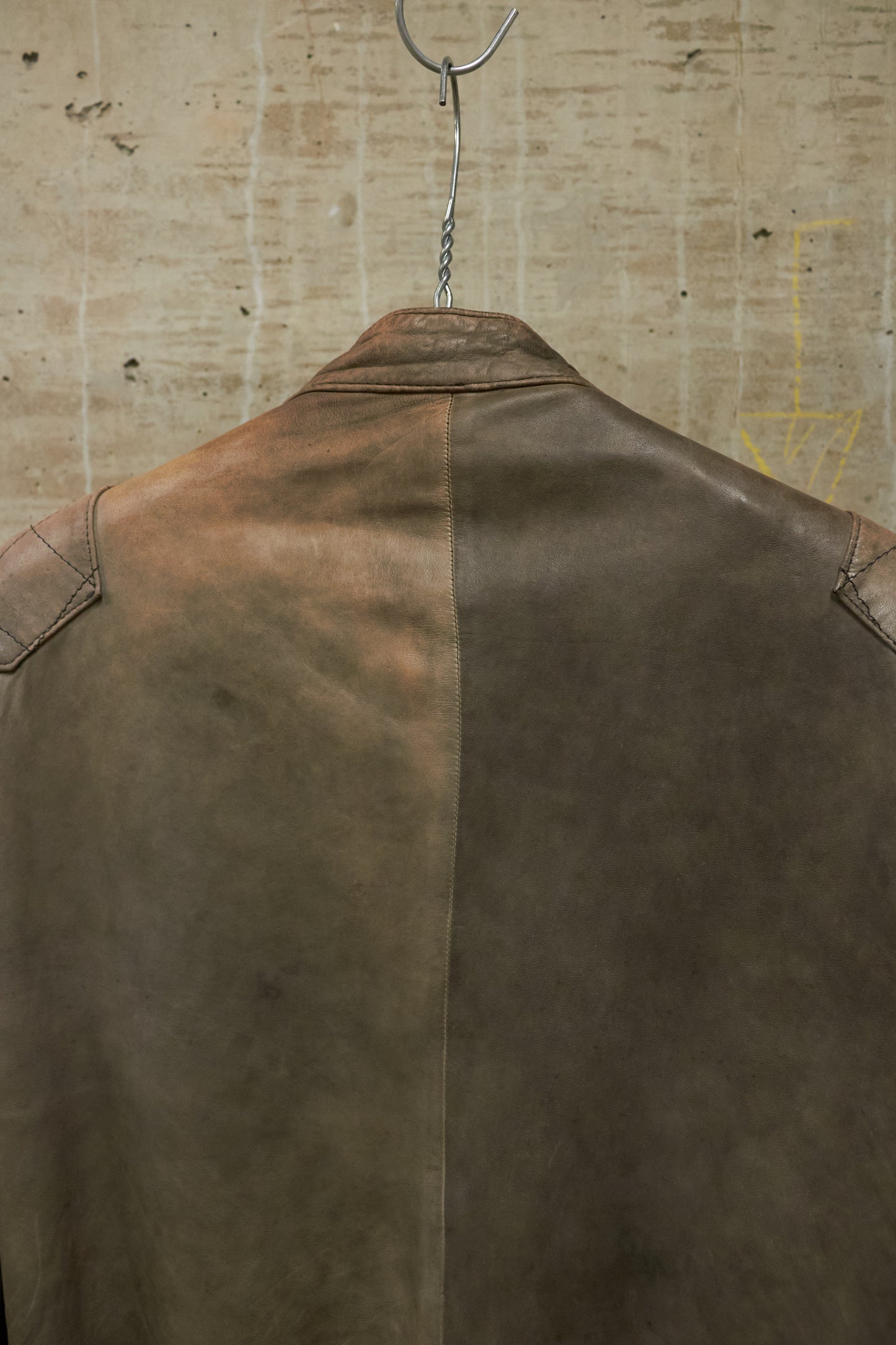 Brown leather jacket on a hanger against a textured beige wall.