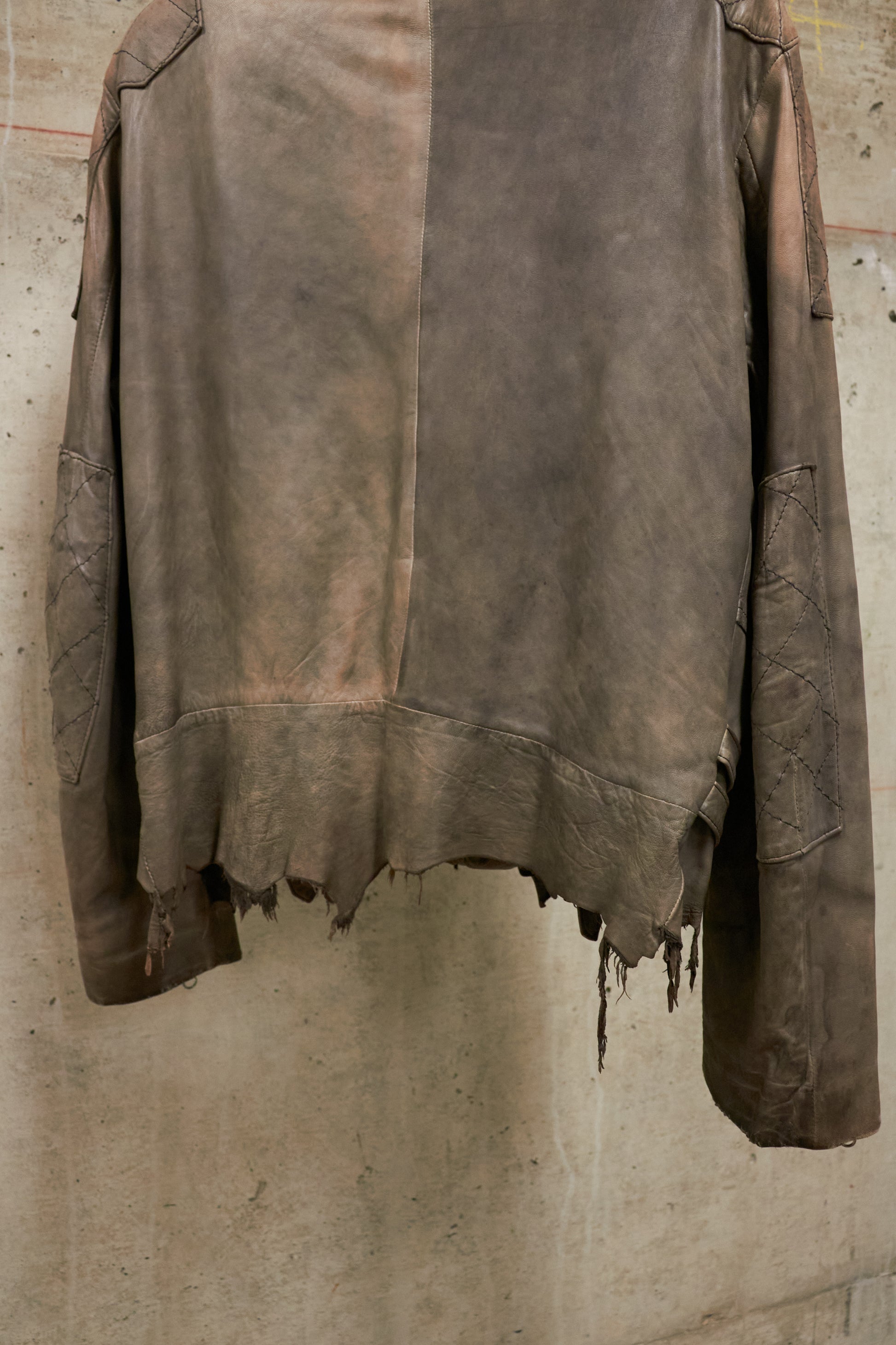 Brown leather jacket hanging against a textured wall