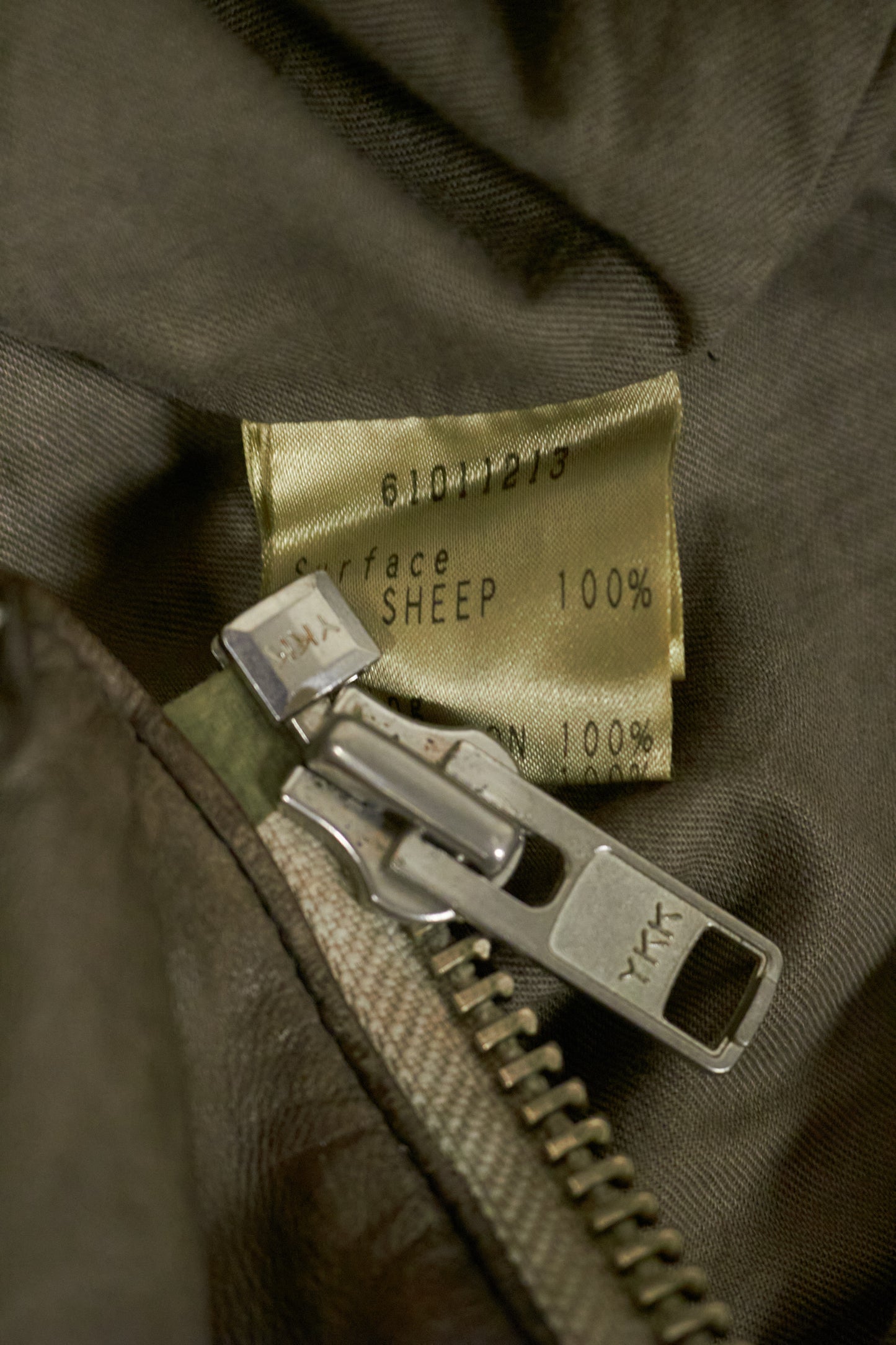 Close-up of a zipper on a brown fabric garment with a label showing 'Sheep 100%'.