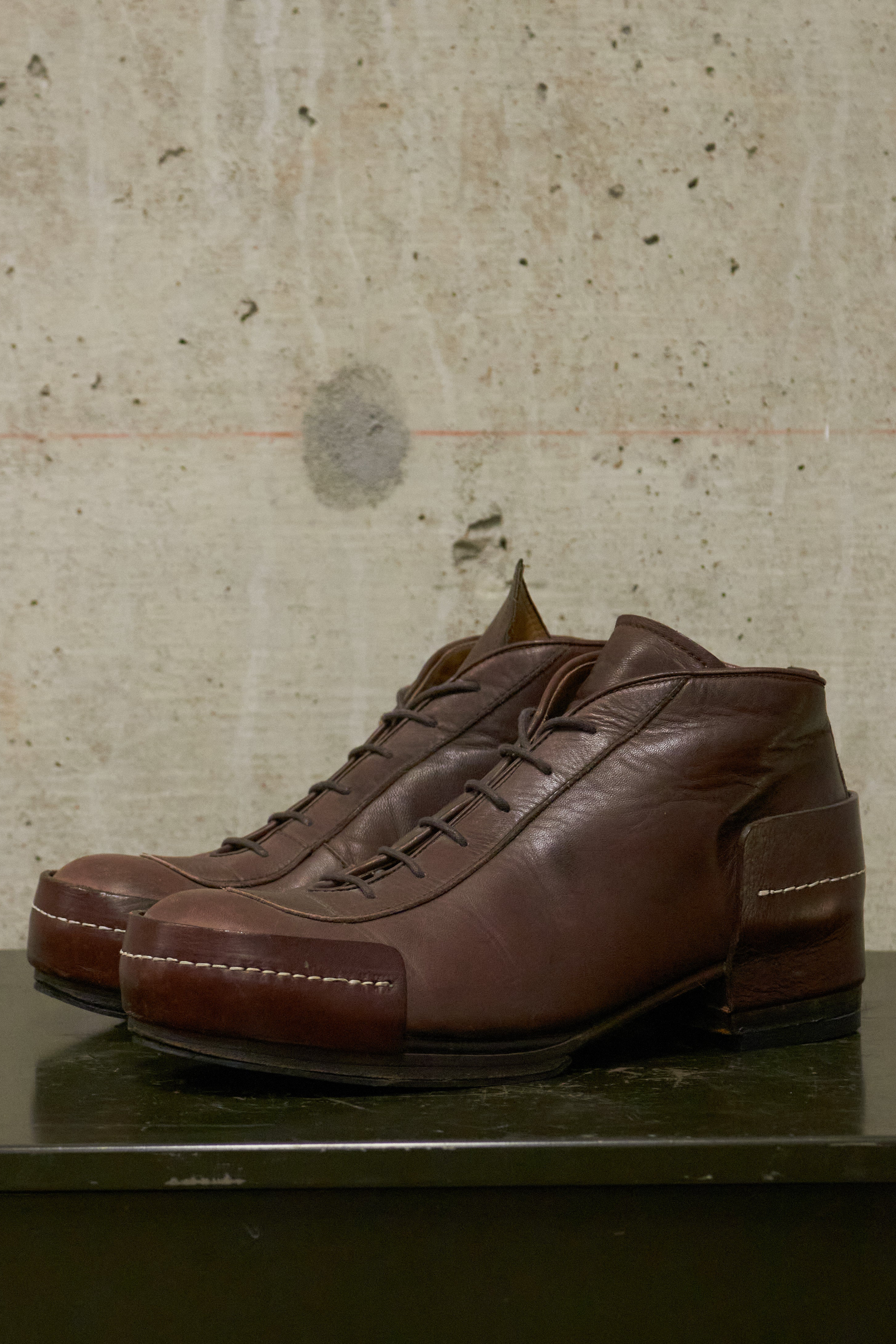 Pair of brown leather shoes on a textured surface with a concrete wall background
