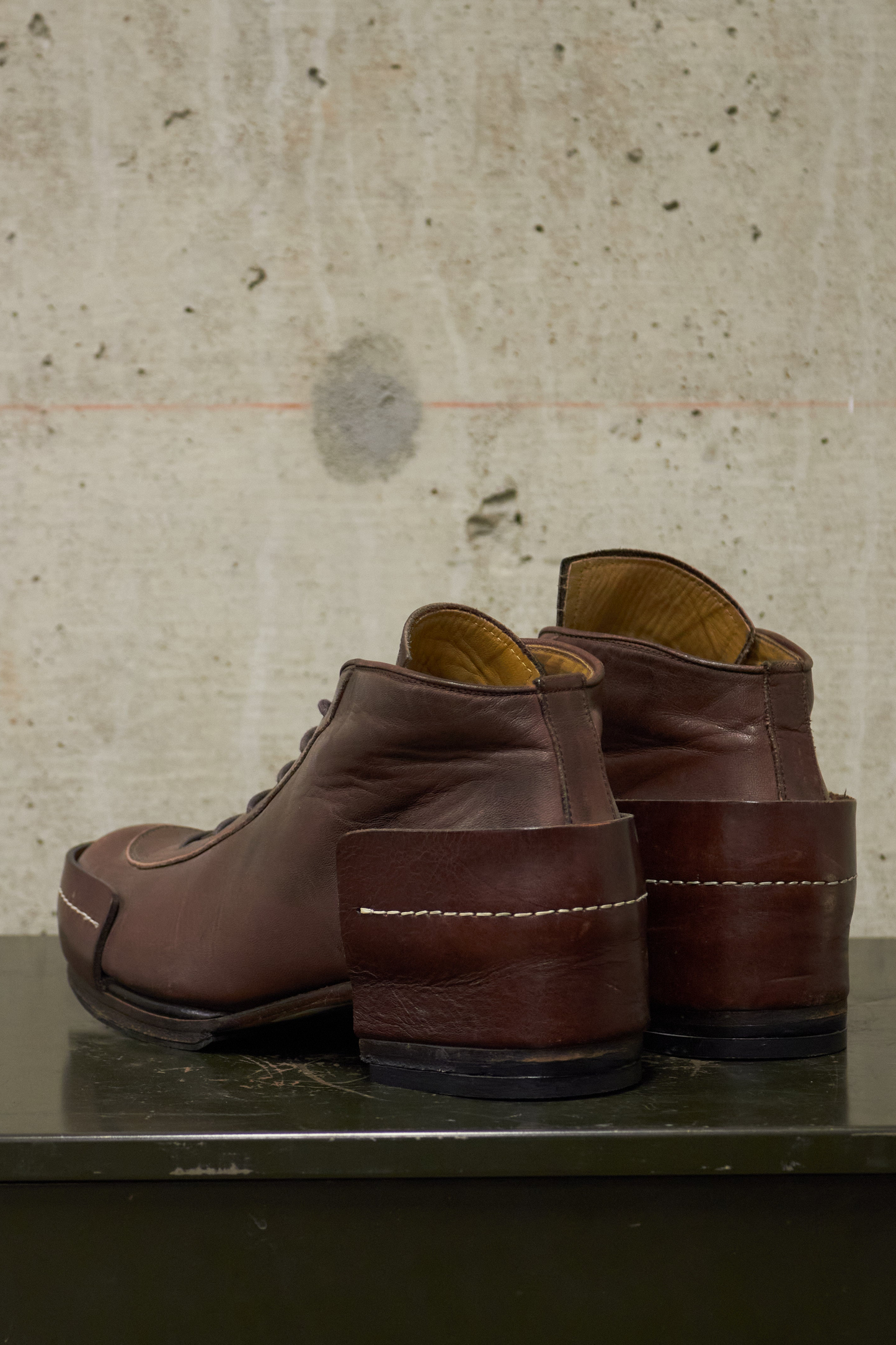 Pair of brown leather shoes on a metallic surface with a textured beige wall background